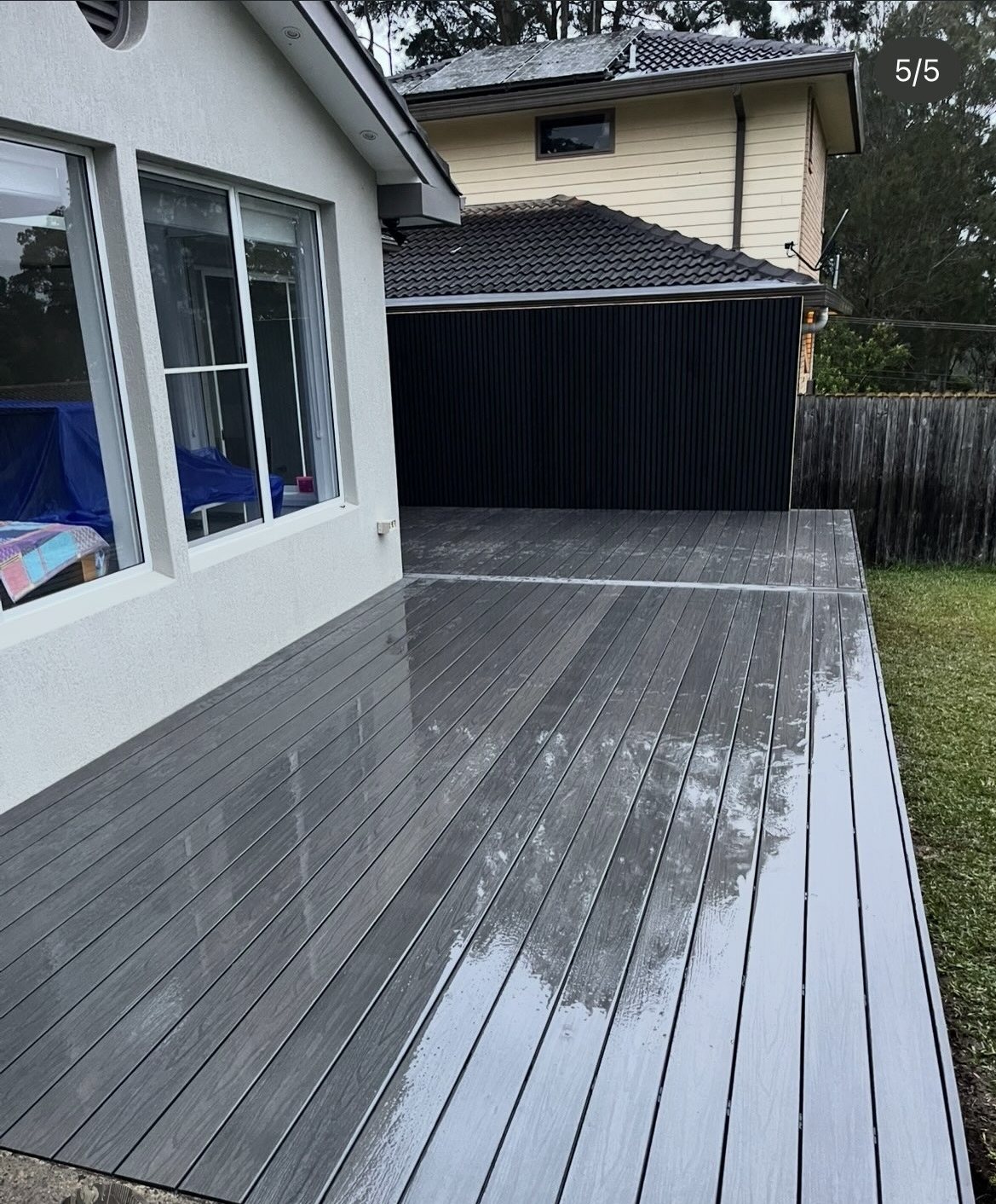 Grey composite deck in the rain, dark slat garage wall
