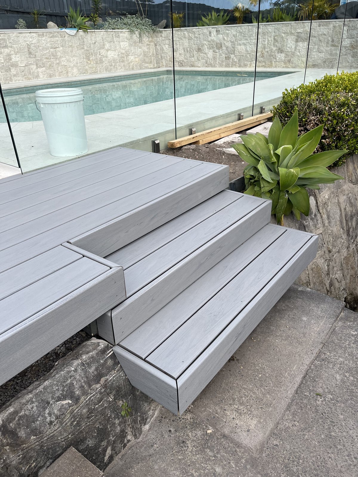 Grey composite deck steps beside a glass-fenced pool
