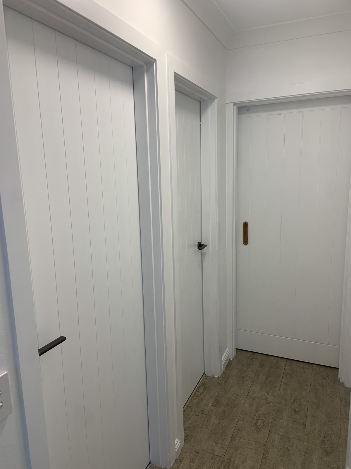 Hallway with three white vertical slat panel doors