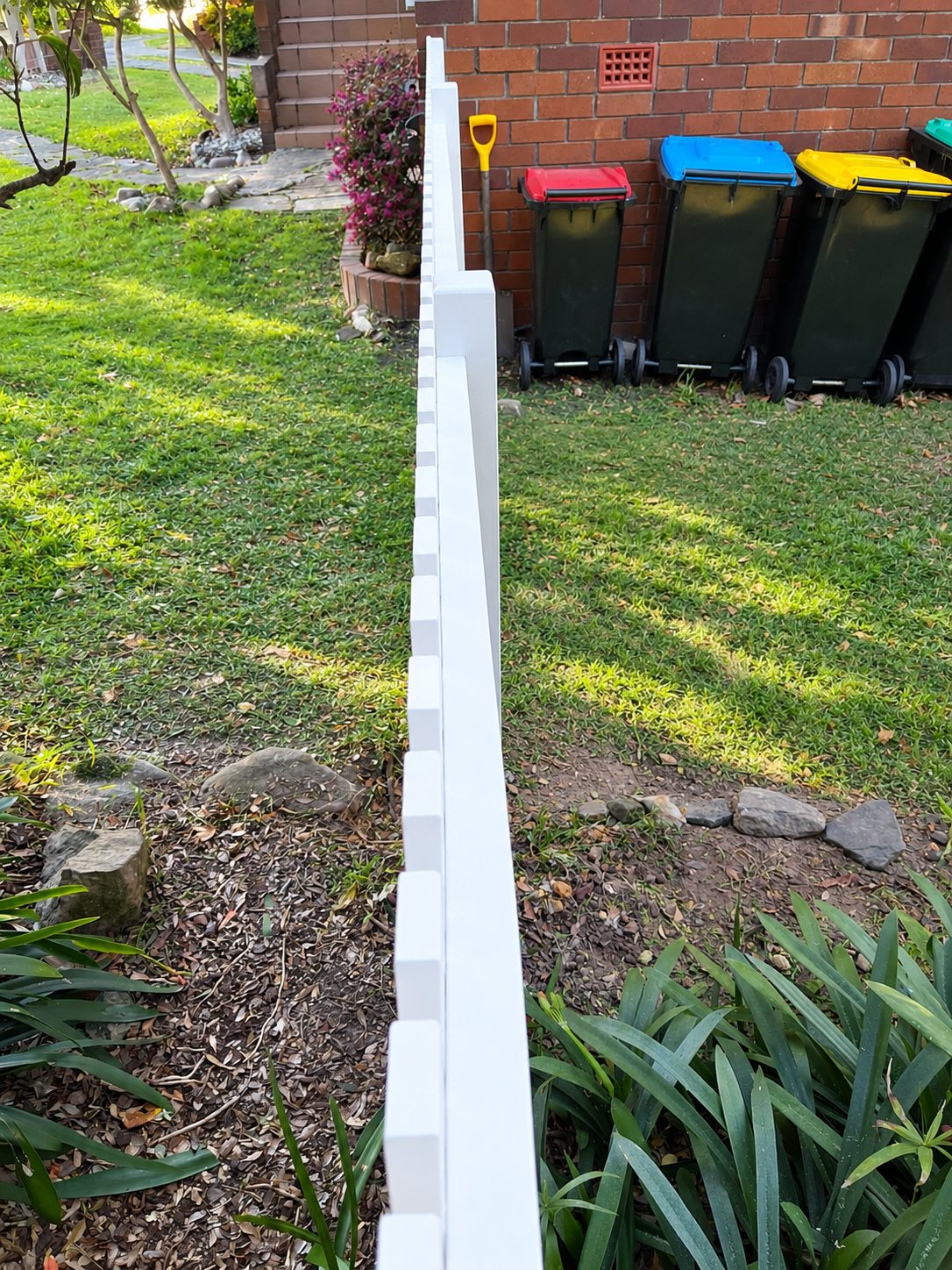 White picket fence along a brick wall with bins