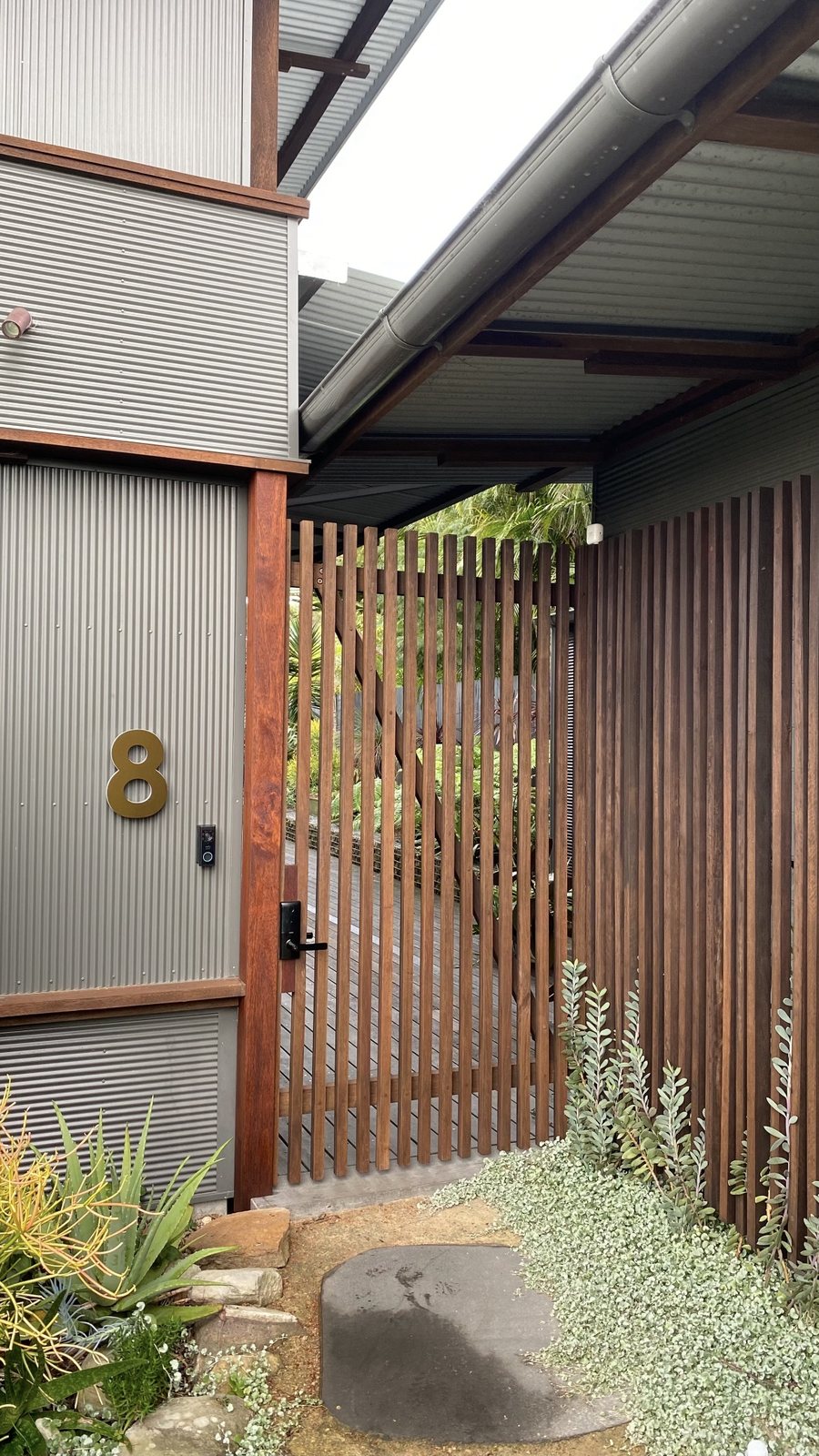 Timber slat gate at a corrugated-clad carport entry